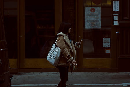 woman standing beside store while using smartphone and holding a cigarette stick thumbnail