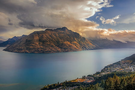 body of water near mountain under white clouds thumbnail