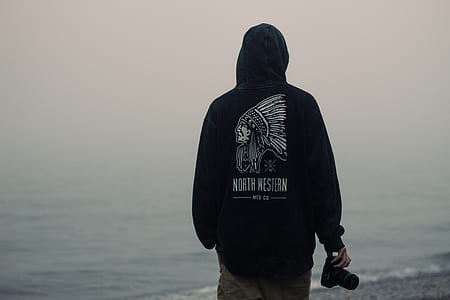 person walking on shore holding black DSLR camera thumbnail