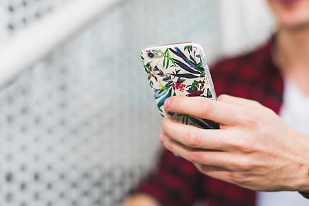 Person Holding Smartphone With White and Green Floral Case thumbnail