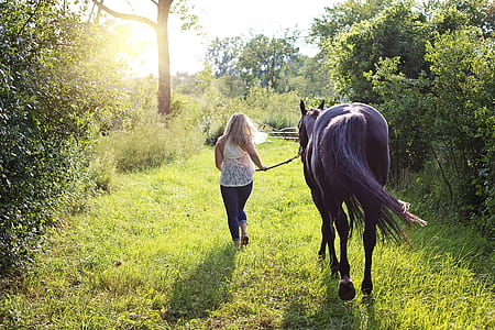 woman wearing white top and blue jeans beside black horse during daytime thumbnail