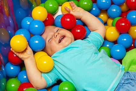 smiling toddler wearing blue t-shirt lying on assorted-color balls thumbnail