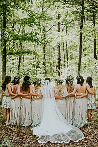 group of people wearing wedding dresses standing against trees thumbnail