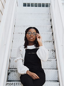 woman holding black framed eyeglasses about to wear while sitting on white metal stairs outdoors thumbnail