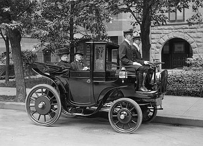 grayscale photograph of three men and one woman riding classic black vehicle thumbnail