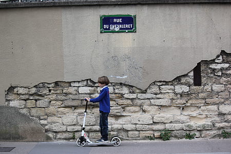 boy in blue long-sleeved shirt standing on kick scooter thumbnail