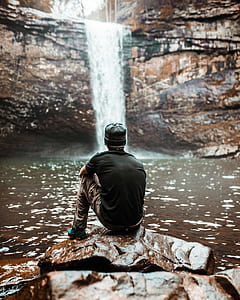 man sitting on rock looking at waterfalls thumbnail