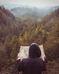 person holding map overlooking green forest at daytime thumbnail