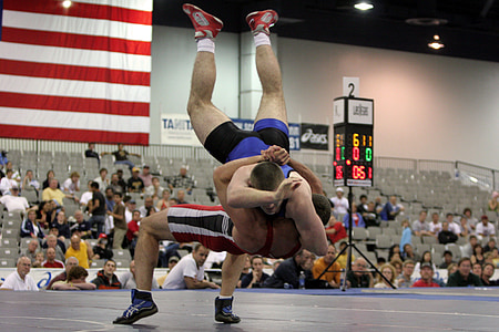 two men wrestling front of people inside building thumbnail