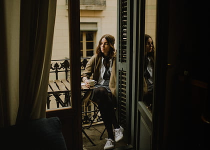 woman sitting on chair while crossing her legs on balcony facing right while having a coffee during daytime thumbnail
