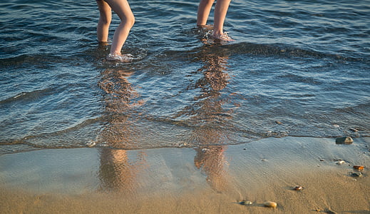 two people standing on body of water near brown sand thumbnail