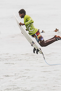 man wearing green long-sleeved shirt and red broadshorts holding white surfboard thumbnail