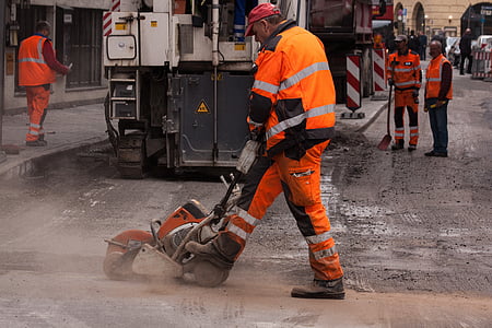 man wearing orange and gray neon jacket and pants using concrete saw on road thumbnail