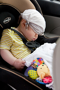 baby wearing yellow and white striped shirt sleeping on brown and black Evenflo booster seat inside car with white handkerchief covered on eyes and hair thumbnail