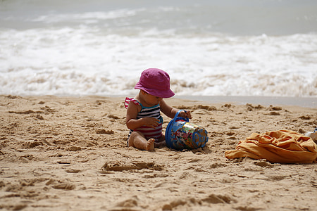 baby wearing purple hat playing sand near ocean at daytime thumbnail