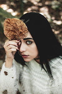 selective focus photography of woman holding dried leaf on her forehead thumbnail