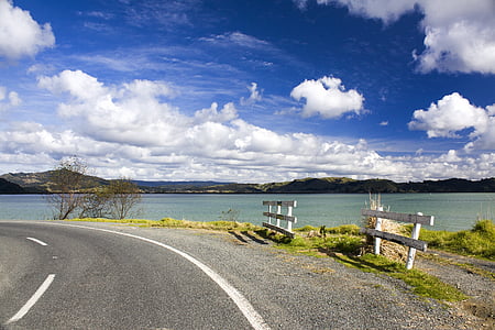 gray concrete road near body of water under cloudy sky thumbnail