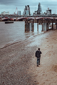 man walking on seashore towards brown wooden dock during daytime thumbnail