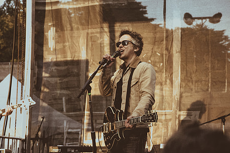 man in brown jacket playing guitar while signing thumbnail