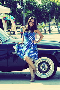 woman in blue and white polka-dot sleeveless dress leaning on black car thumbnail