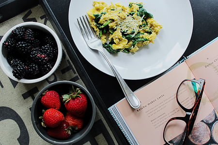 two bowls of blackberries and strawberries next to plate with dish and fork beside opened book with eyeglasses on top thumbnail