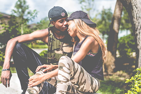 man and woman with black baseball caps sits near green leaf trees during daytime thumbnail