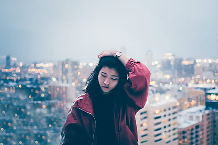 woman in red zip-up jacket holding her hair under cloudy sky during daytime thumbnail
