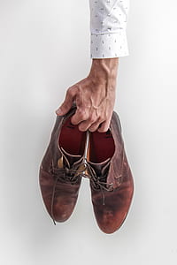 person in white and black long-sleeved shirt holding pair of brown leather lace-up dress shoes thumbnail