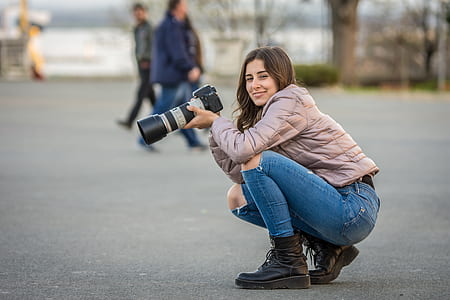 woman in gray jacket holding DSLR camera thumbnail