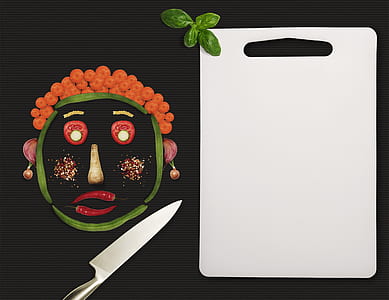 face-shaped sliced vegetables beside white chopping board and kitchen knife thumbnail