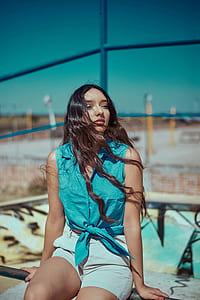 woman wearing teal vest and white short shorts sitting on brown metal bar during daytime thumbnail