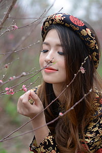 close-up photo of woman in brown and black floral long-sleeved dress near pink petaled flower during daytime thumbnail