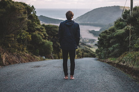 man standing on black asphalt road towards mountain thumbnail