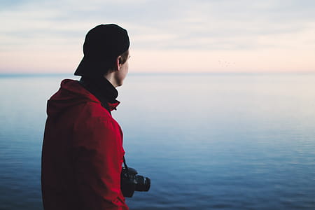 Man in Red Jacket Standing Near Body of Water thumbnail