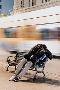 long exposure photography of sitting person wearing black hoodie, khaki pants and sneakers on black metal bench beside street thumbnail