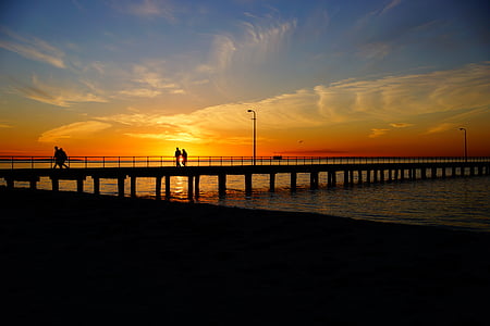 silhouette of couple walking on sea dock during golden hour thumbnail