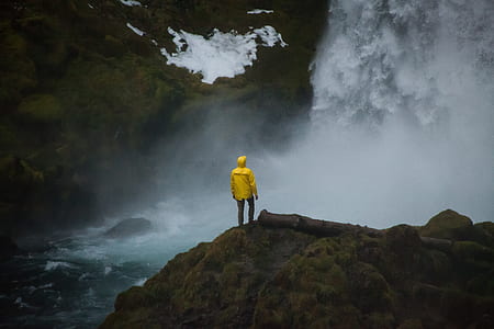 person standing on brown rock formation in front of waterfalls thumbnail