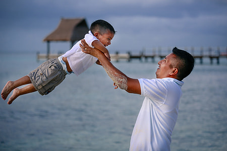 shallow focus photography of man carrying his son on beach during day time thumbnail