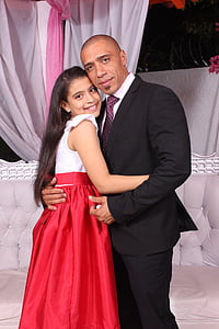 man in black suit and dress pants hugging girl in red and white dress thumbnail