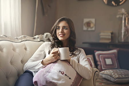 woman sitting on tufted white sofa while holding white ceramic mug thumbnail