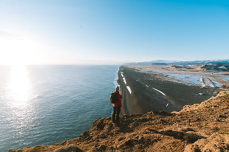 person standing on cliff viewing sea under white and blue sky during daytime thumbnail