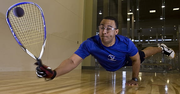 man holding purple and white racquetball racket on brown wooden floor thumbnail