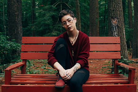 woman wearing red sweater and black jeans sitting on red wooden bench in fores at daytime thumbnail