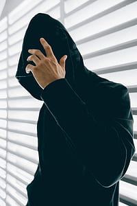man wearing black velvet hoodie standing beside window blinds thumbnail