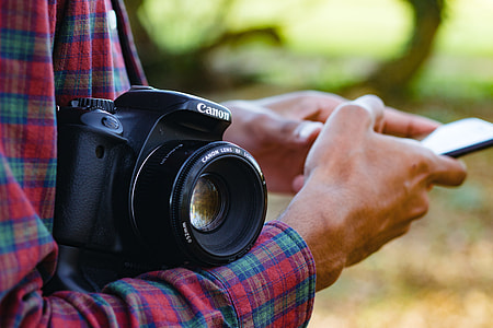 person with black Canon DSLR camera on arm while holding smartphone thumbnail