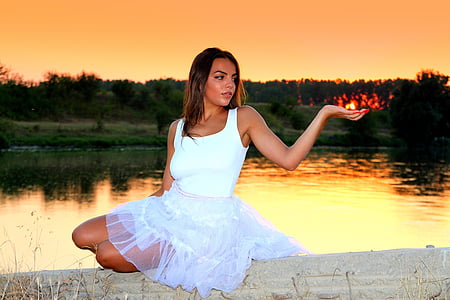 woman wearing white sleeveless dress sitting over lake during sunset thumbnail
