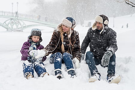man, woman, and boy sitting on snow ground making snowballs thumbnail