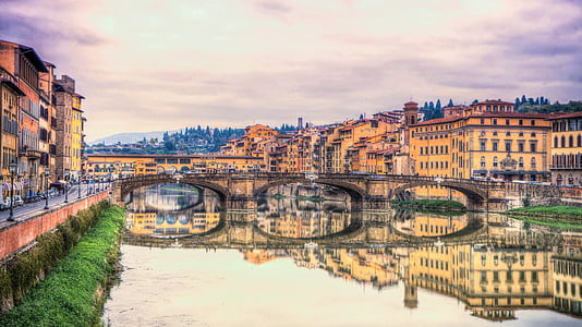 photography of brown concrete bridge near brown painted building and body of water under white sky thumbnail
