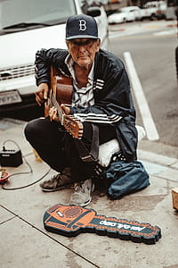 man sitting on pavement holding guitar thumbnail