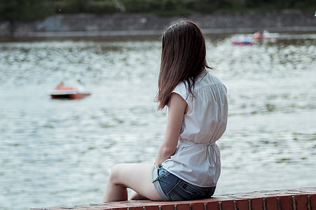 woman sitting on concrete bench near body of water thumbnail